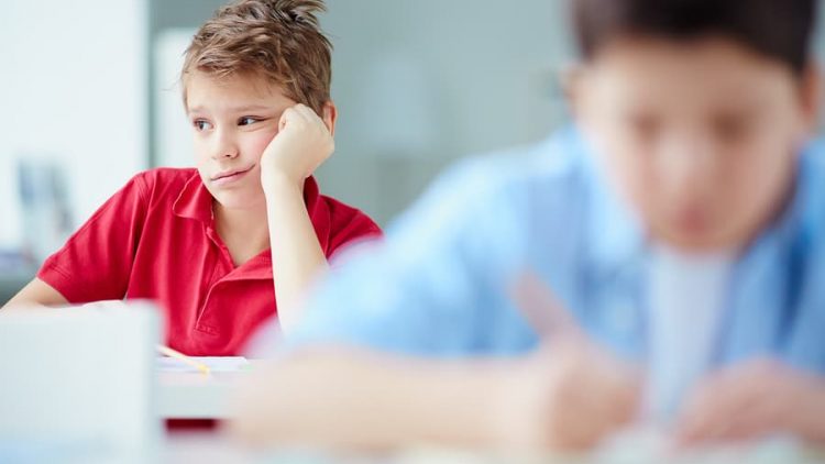 image of grade school boy sitting at his desk looking sad and distracted. this image is being used to illustrate the importance of effective communication with your grade schooler and working with ogborne law firm, a phoenix based family lawyer, during your collaborative divorce.