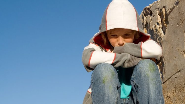 an image of a sad tween boy wearing a hoodie sitting alone framed against a blue sky. this image is being used to convey the impact of divorce on tweens and the important of understanding how to communicate with them and how ogborne law, phoenix based family law firm, can help you communicate with your tween during your collaborative divorce.