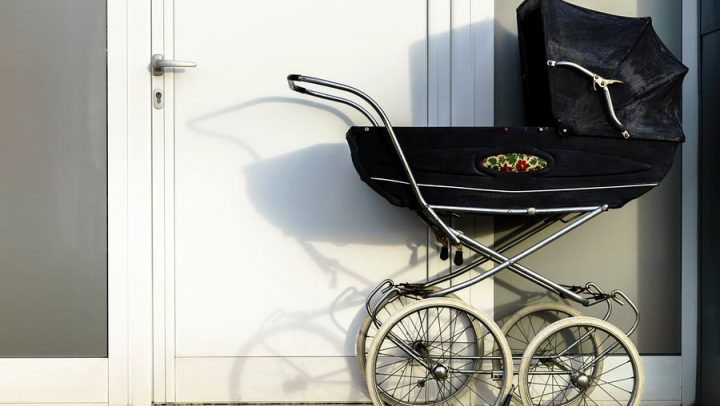 retro black baby carriage against a white door. this image is being used to convey that things like having a new baby can change your estate plan and that you need to update it by working with ogborne law, phoenix estate planning attorney.