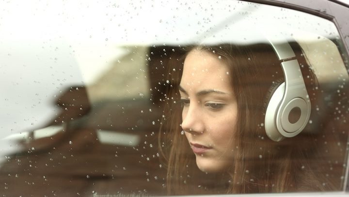 teenaged girl in her parents car listening to headphones with a sad expression on her face. this image is being used to express how kids feelings can change during divorce and that working with ogborne law, phoenix collaborative divorce attorney, can help you communicate better with your kids during divorce.