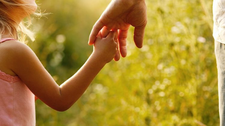 a man holding the hand of his little girl while on a walk through the tall grass. this image is being used to convey the importance of having a parenting plan in place and why ogborne law, phoenix family law firm, focuses on ensuring that you and your ex-spouse create a parenting plan that focuses on the success of the child.